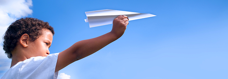Foster boy flies paper airplane in a blue sky