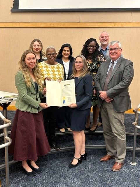 County of Sonoma Board of Supervisors and Commissioners on the Commission on the Status of Women posing with a gold resolution at the Chambers